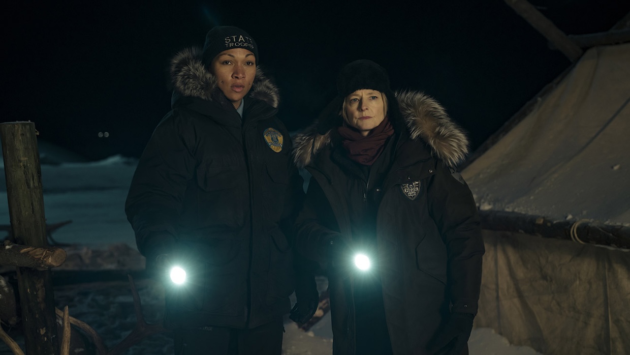 Two women shine their flashlights while standing in a dark, snowy landscape.