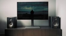 A television displaying na image during daytime with of a man on a dark beach in a living room.