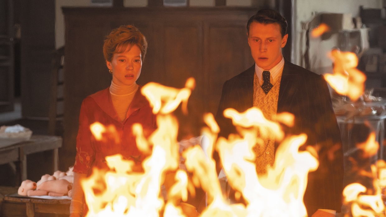 A woman and man stare at a fire in a doll factory.