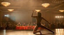 A female bodybuilder flexes on stage before a table of judges.
