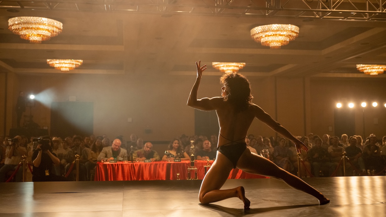A female bodybuilder flexes on stage before a table of judges.