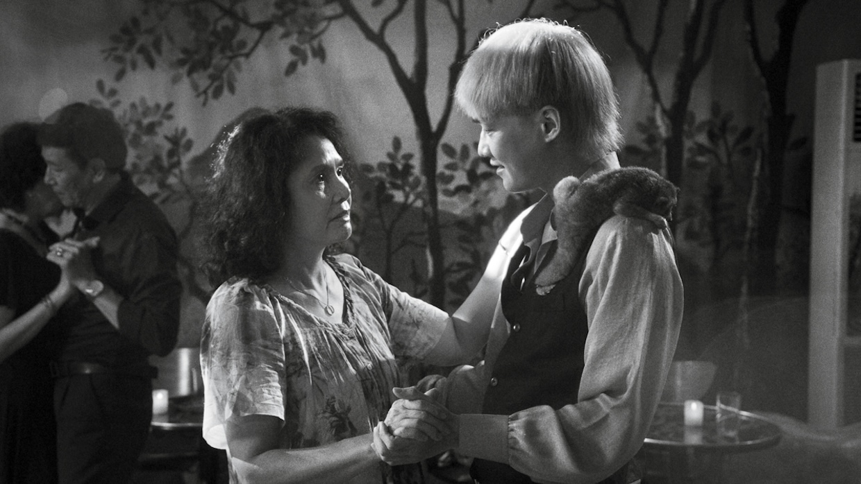 A middle-aged woman dances with a younger man who has a primate on his left shoulder.