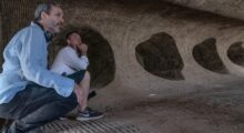 Two white men crouch in a cave.