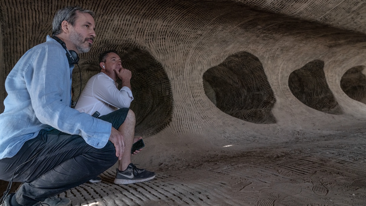 Two white men crouch in a cave.