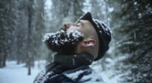 A bearded man in a Union army uniform stands with his eyes closed in the snow.