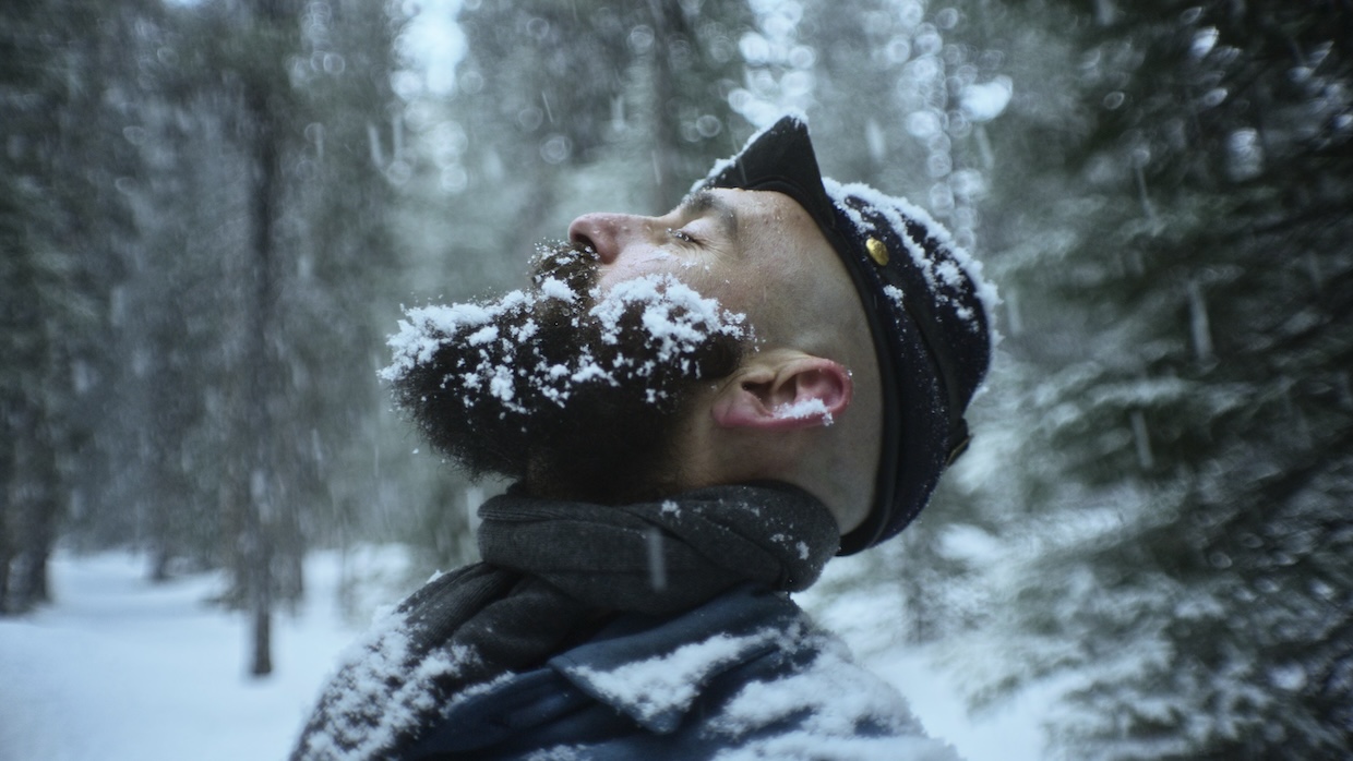 A bearded man in a Union army uniform stands with his eyes closed in the snow.