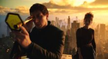A man looks over a city landscape through a telescope at sunset while a woman stands behind him.