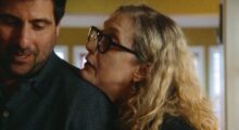 A middle-aged white woman leans her chin on a younger white man's shoulder.