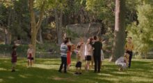 A large extended family of white people mills around a sunny, park-like landscape.