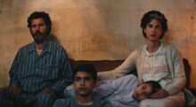 A Palestinian family sits in their living room, worried expressions on all of their faces.