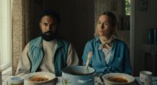 A couple sits side-by-side at a table with bowls of soup.