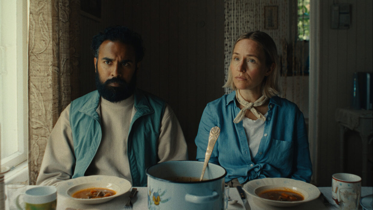 A couple sits side-by-side at a table with bowls of soup.