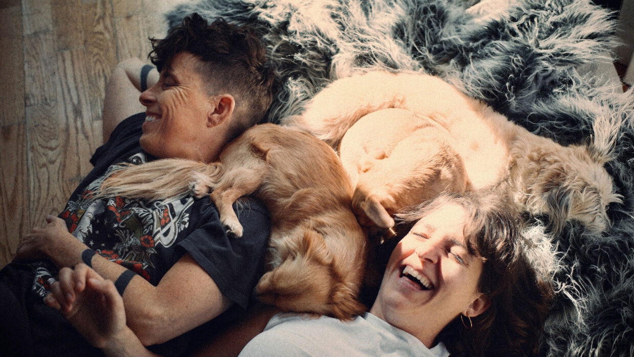 Two people are lying on the floor laughing while a small dog sleeps between them.