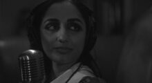 Black-and-white close-up of a women wearing headphones in front of a microphone.