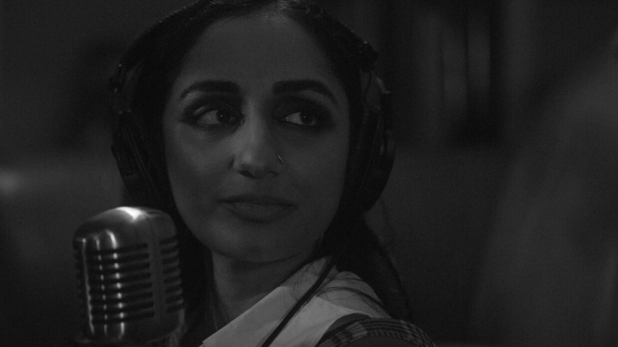 Black-and-white close-up of a women wearing headphones in front of a microphone.