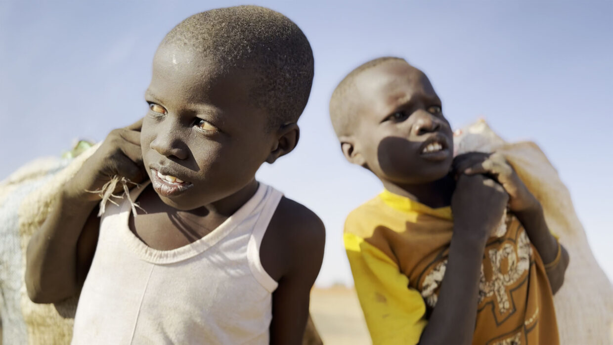 Two-shot of young Sudanese boys comparing bags over their shoulders.