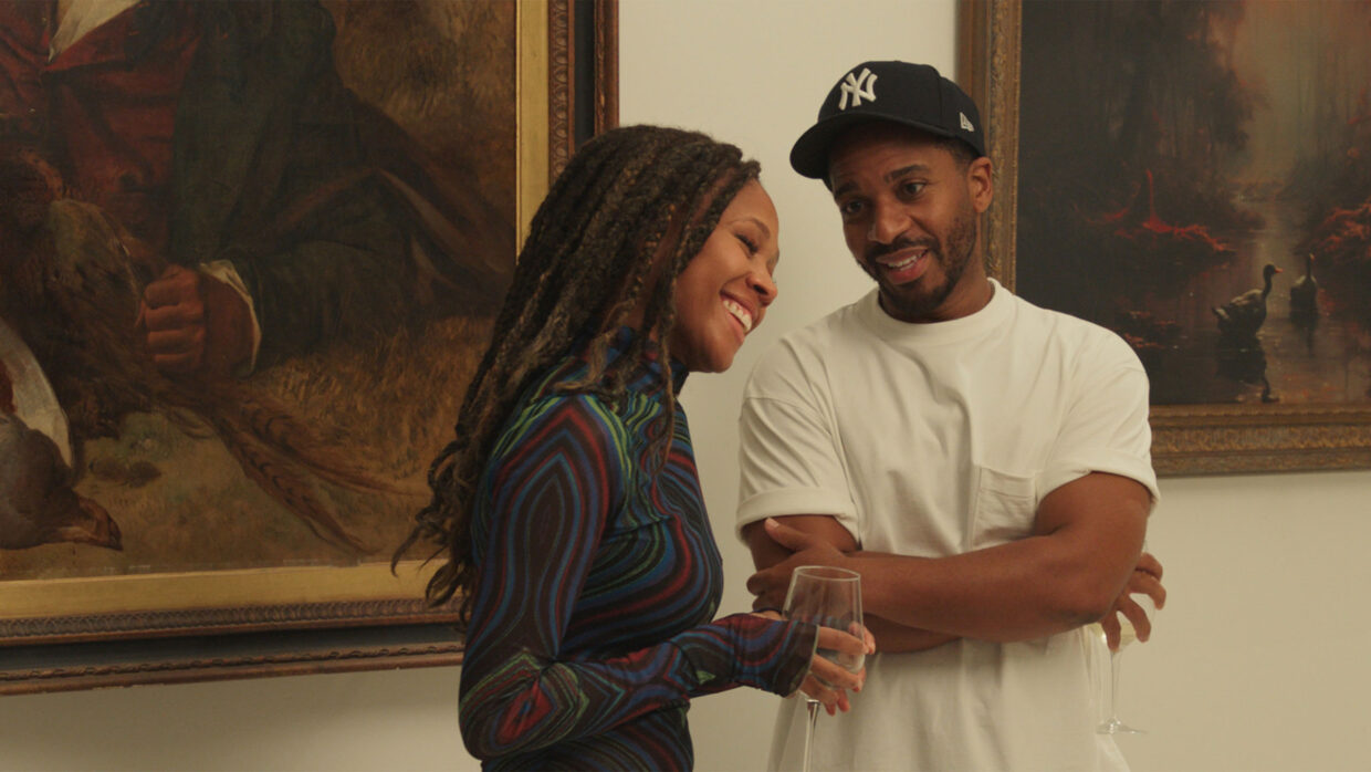 A Black man in a Yankees cap and a Black woman are standing together in an art gallery.