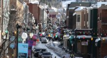 A snowy, sunny street crowded with cars in a mountain town.