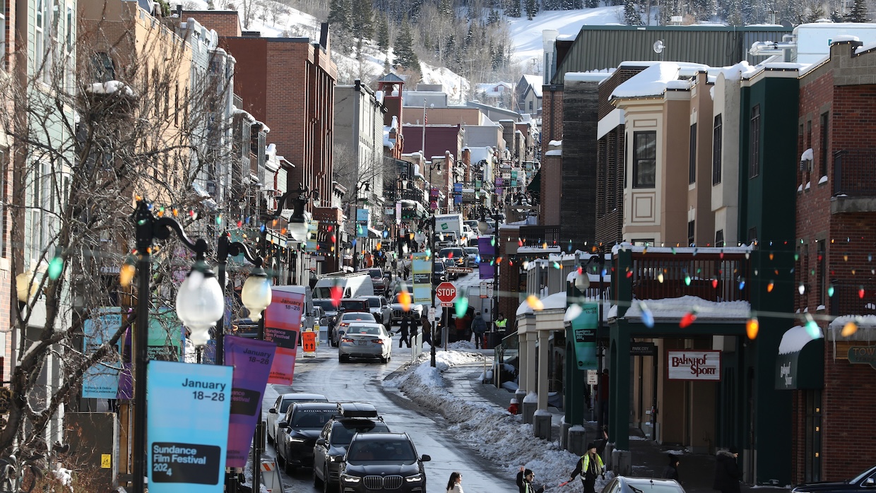 A snowy, sunny street crowded with cars in a mountain town.
