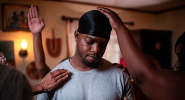A Black man is being consoled or congratulated by friends around him.