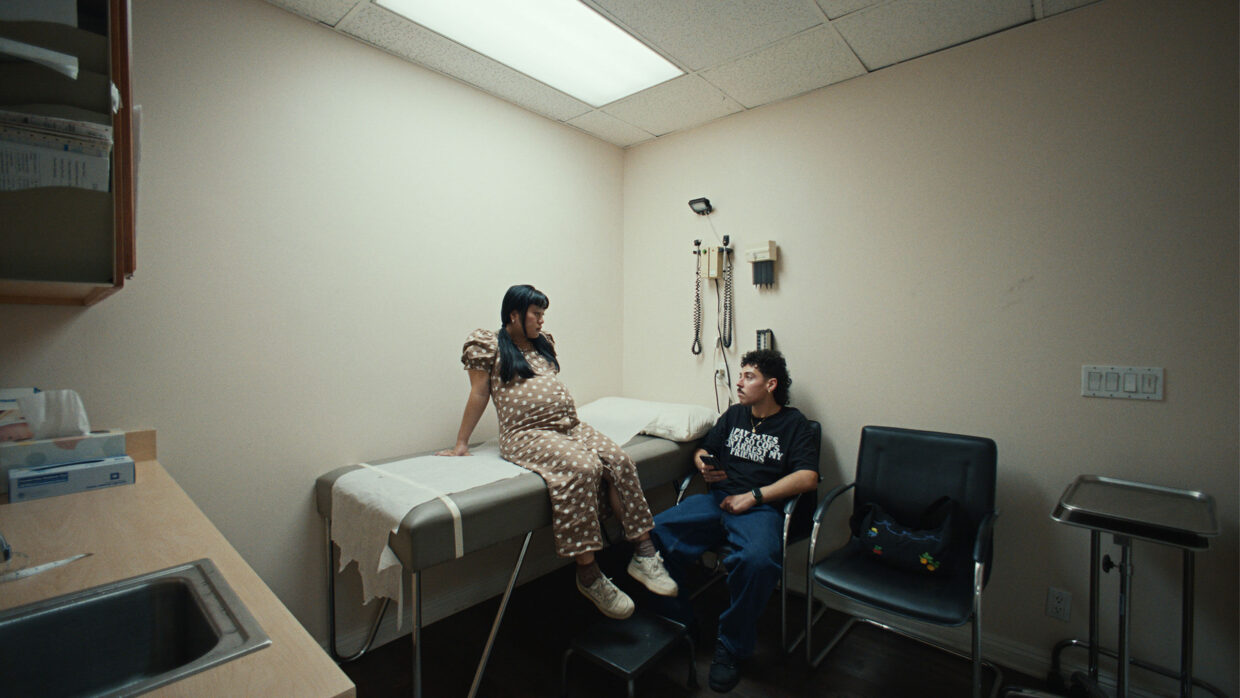 A pregnant woman is sitting on a table in a doctor's office while a man sits next to her on a chair.