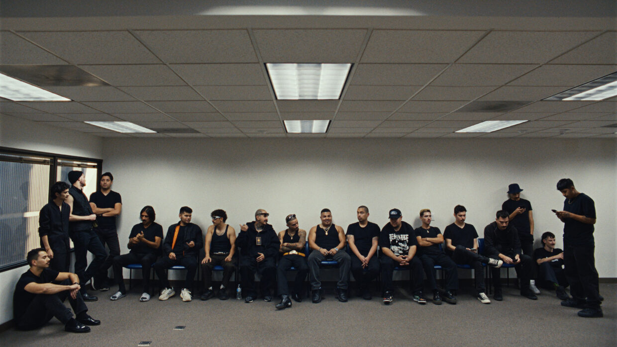 Wide shot of a large group of men sitting or standing along a wall.