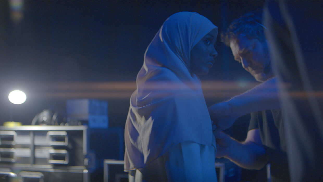 A white man is fastening something on a woman's hijab.