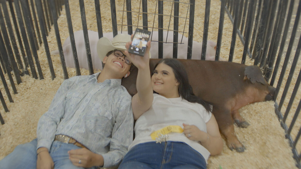 Two high school students take a selfie with two pigs.