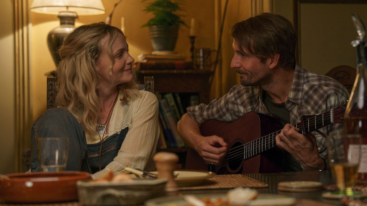 Carey Mulligan and Tom Basden, who is holding a guitar as they sit at a table.