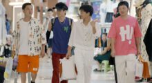 Four young men, all sporting trendy garb, walk through a mall with shopping bags.
