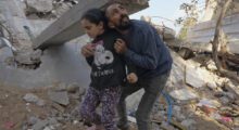 A Palestinian man holds a young girl amid rubble