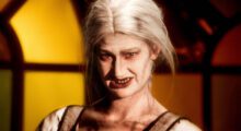 A woman with decaying teeth and platinum hair grins.