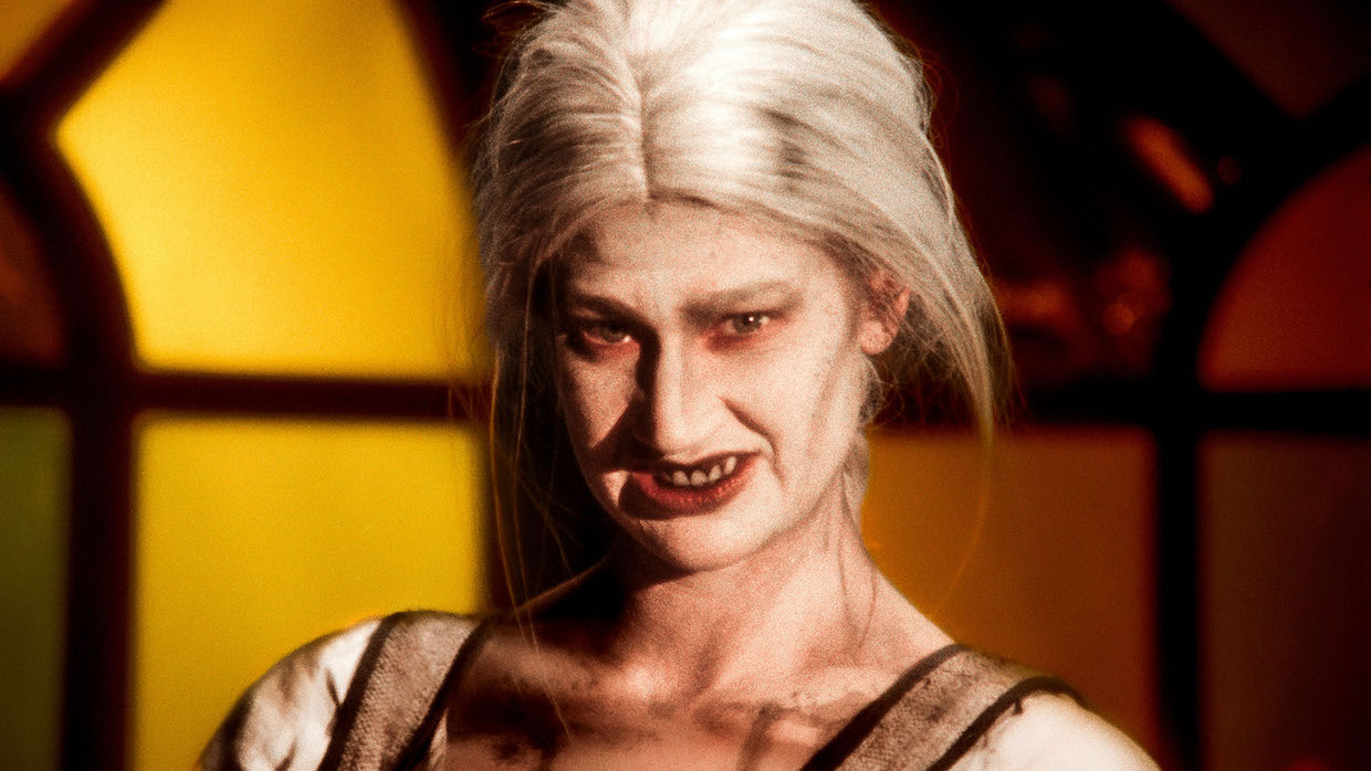 A woman with decaying teeth and platinum hair grins.