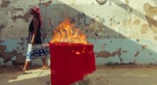 A woman walks past a table outside whose tablecloth is on fire.
