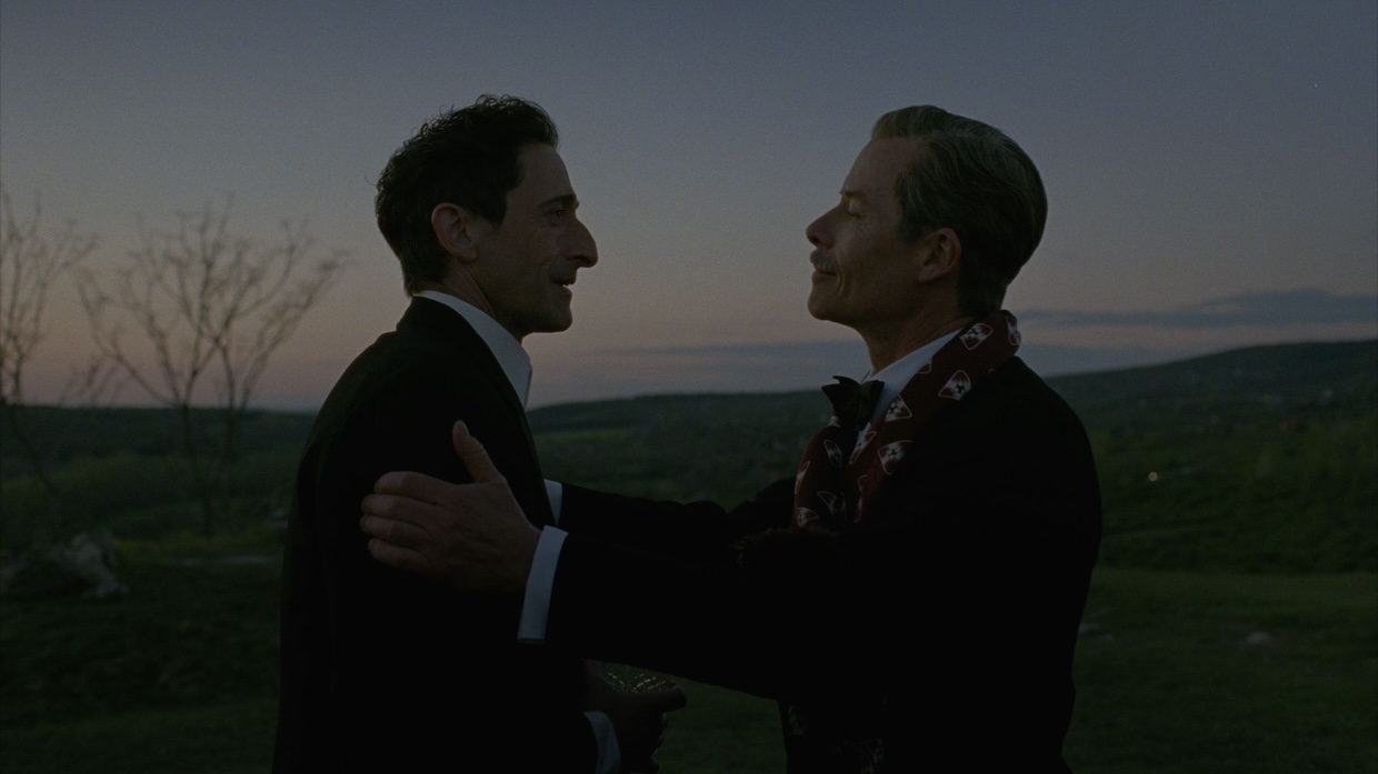 Two men stand on a mountain before a sunset.