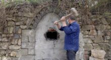 A man takes a hammer to a stone wall.