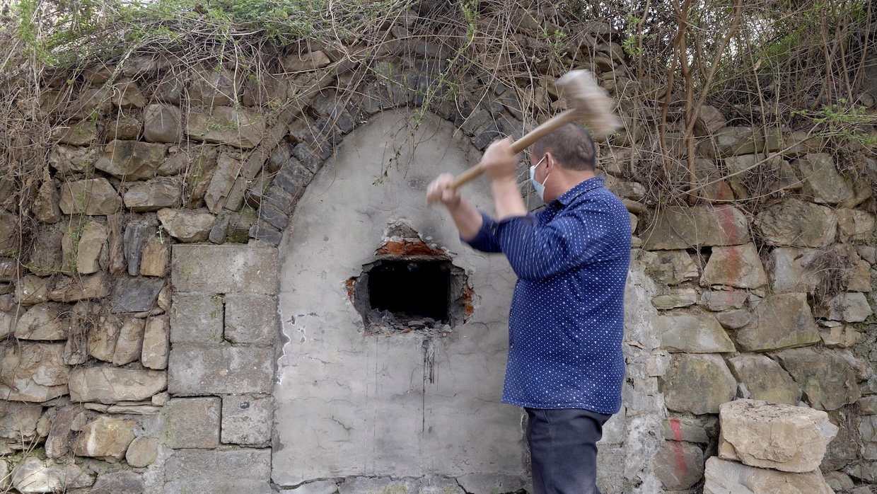 A man takes a hammer to a stone wall.