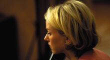 A blond woman holds a phone to her right ear.