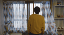 A man in a yellow sweater stares out a window.
