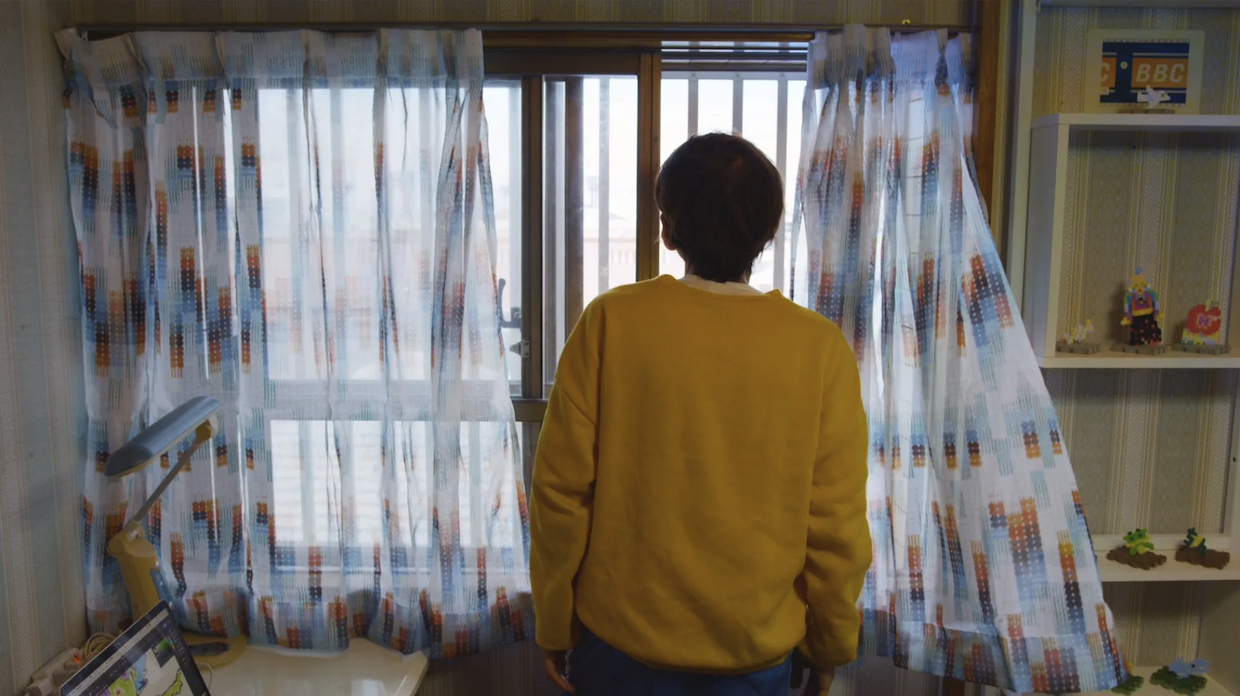 A man in a yellow sweater stares out a window.