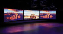 Three large monitors display AI-generated images of a desert in a gallery.