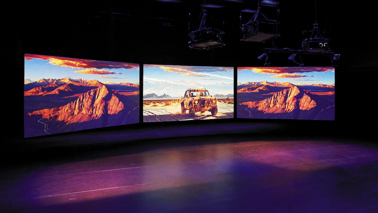 Three large monitors display AI-generated images of a desert in a gallery.