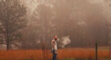 A man in an undershirt stands in a foggy field