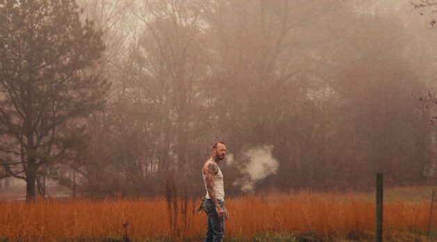 A man in an undershirt stands in a foggy field