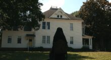 A woman in a full black veil stands outside a house in daylight.