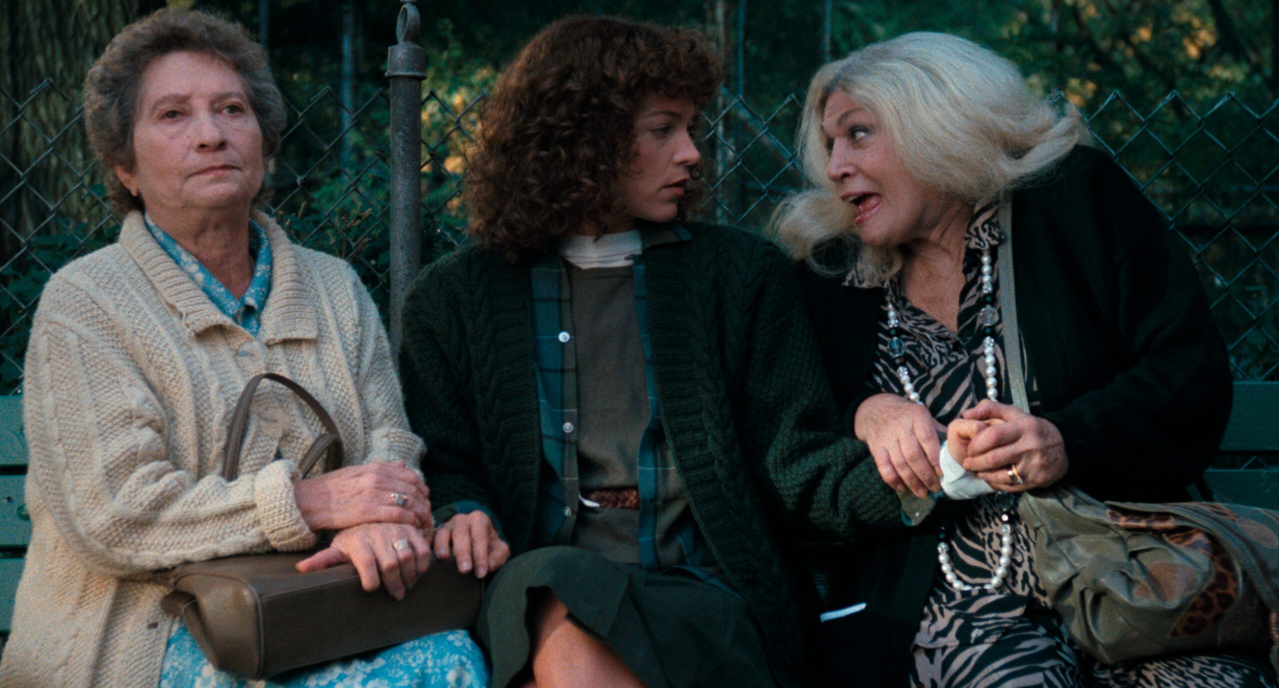 Three women sit on a park bench.