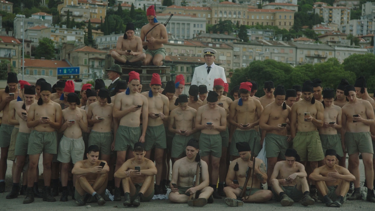 Dressed in anachronistic Italian uniforms, a group of young men stare at their smartphones.