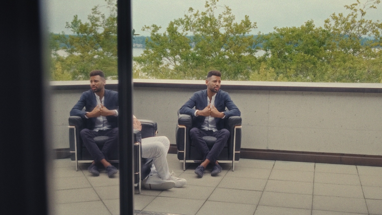 A man in a business casual suit sits in a chair on an outside patio.