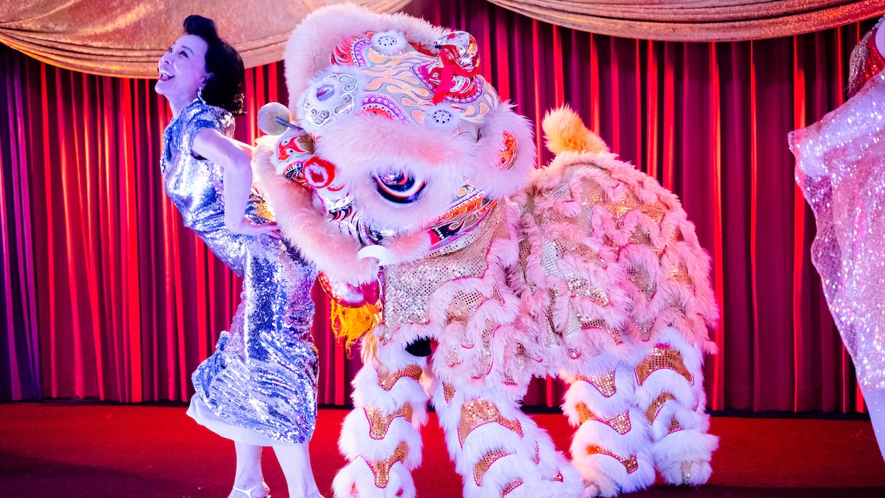 A woman and a Chinese dragon costume stand onstage.