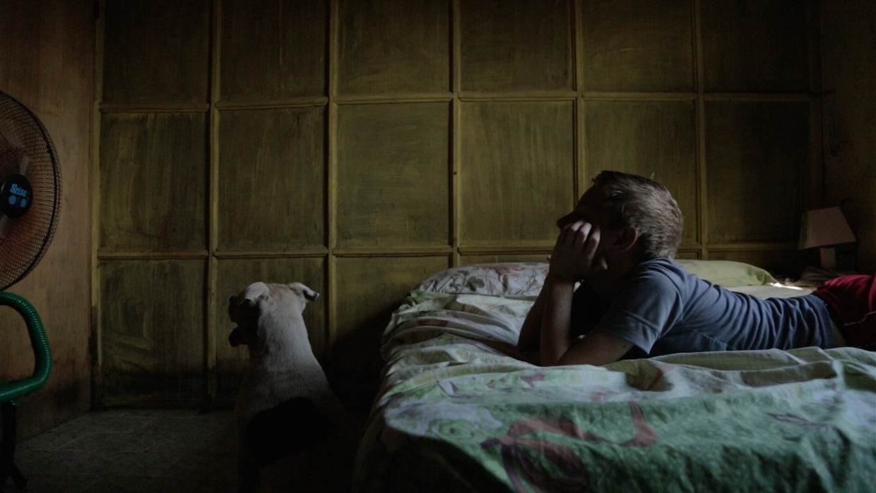A boy rests on a bed with his dog next to him in a dark room.